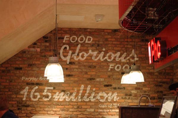 Large white graphics painted on a brick wall. Featuring the slogan 'Food Glorious food' and underneath 'Everyday Britain drinks 165 million cups of Tea