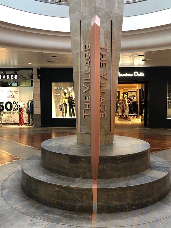 Side on view of the totem sign at the entrance to The Village Arcade, flanked by branding on the column.