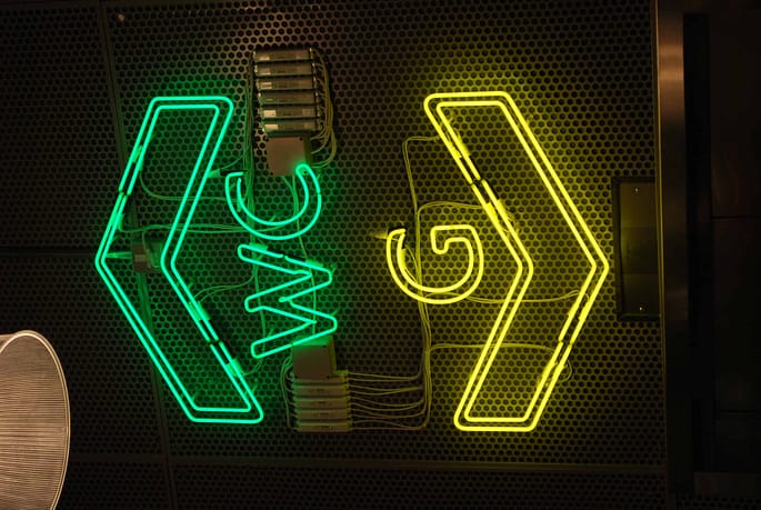 Large neon sign placed over the lift. at the top is the outline of a green arrow head, pointing upwards with the word WC underneath. Below this is yellow is the letter G followed by a downward pointing arrow head
