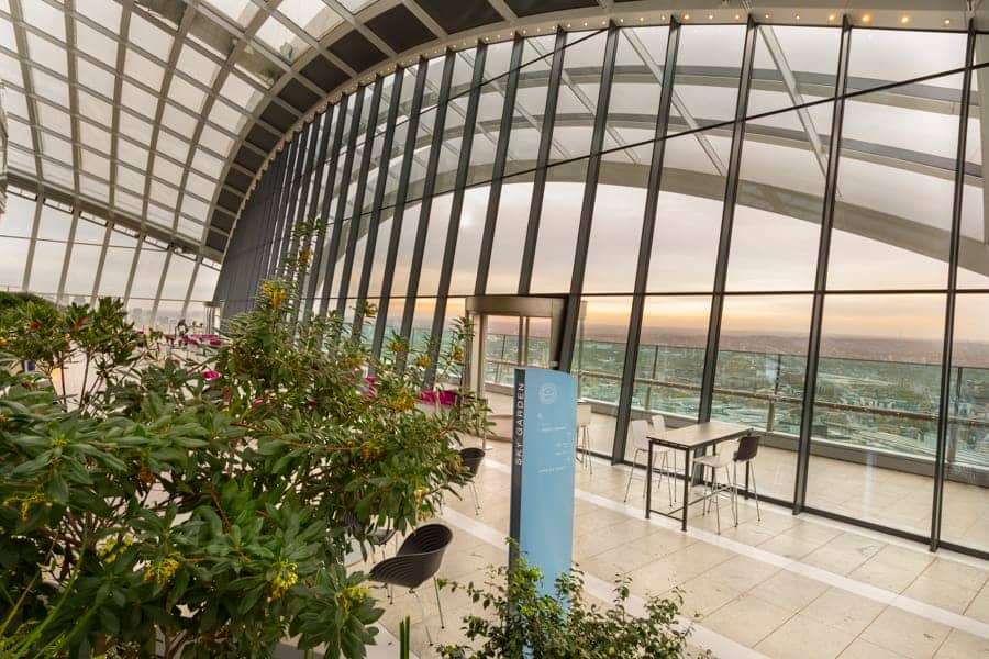 View of a totem sign through the foliage to views of London beyond in the Sky Garden visitor attraction